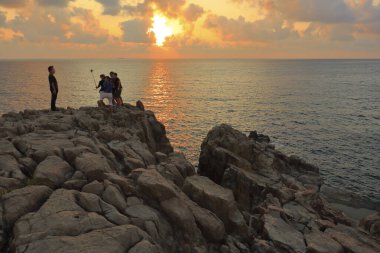 Turistler kayaların üzerinde durur ve güzel günbatımının tadını çıkarırlar. 