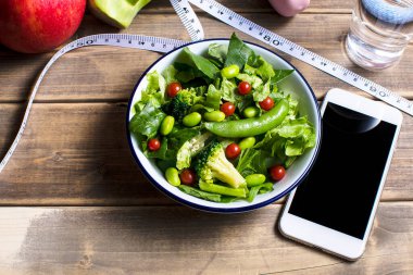 Akıllı telefon ve mezura yakınında sağlıklı bir salata kasesi.