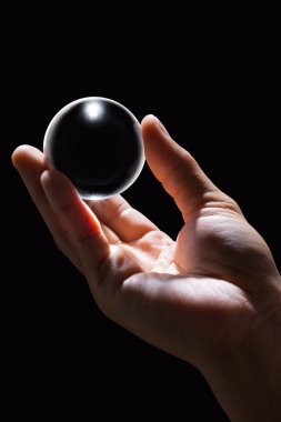 Siyah zemin üzerinde şeffaf cam top tutan el.
