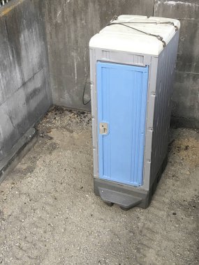 Taşınabilir tuvalet gri beton duvarda duruyor.