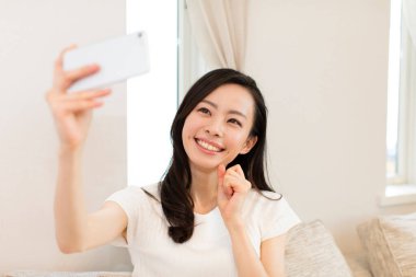 Mutlu Asyalı kadın evde selfie çekiyor.