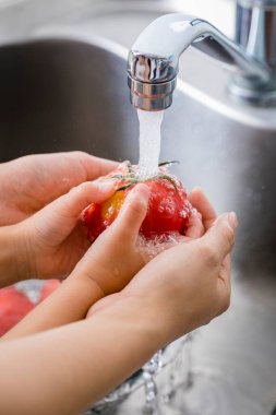 Musluğun altında taze kırmızı domatesleri yıkıyorum.