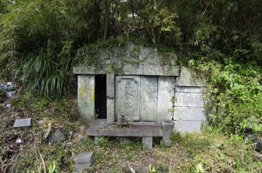 Açık havada yoğun yeşil yapraklarla çevrili yıpranmış taş yapı.