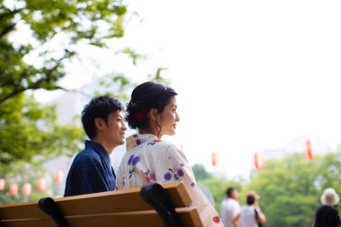 Geleneksel kimono giyen genç Japon çift yaz parkında bankta oturuyor.