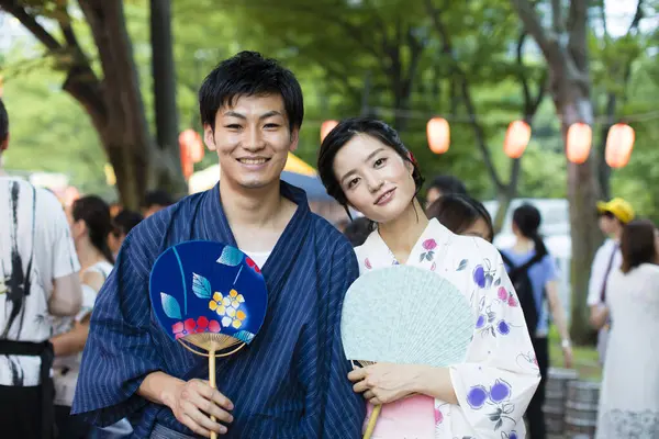young Japanese couple wearing traditional kimono and holding Asian fans in the park