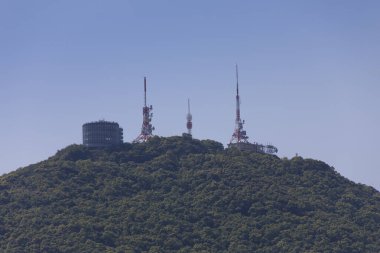 Yeşil dağın tepesinde duran iletişim kuleleri