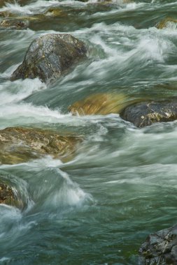 Nehirdeki kayaların üzerine su sıçrıyor.