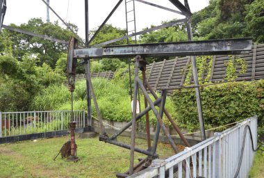 Yeşil çalıların yanında duran eski metal yağ pompacısı.