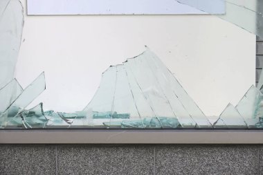 Kırık cam parçaları gri beton duvara saçılmış.