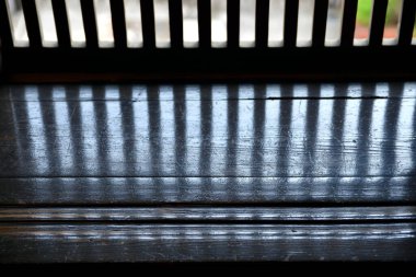 Korkulukların dikey gölgeleri karanlık, yansıtıcı ahşap bir yüzey boyunca dökülür..