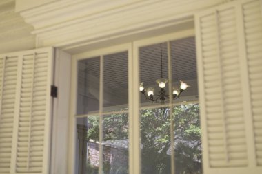 Beyaz panjurlu ve içinde avize olan pencere.