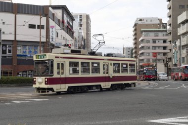 Tramvay gündüz Japon şehrinde caddeden karşıya geçiyor. 
