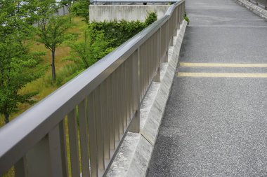 Çevresinde yeşil ağaçlar olan boş patikanın yanında metal korkuluklar.