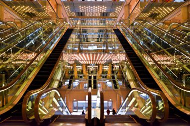 Altın kaplamalı sayısız yürüyen merdiven modern bir binanın çok katlı avlusundan yükseliyor..