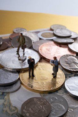 Bozuk para, bitcoin ve altın külçelerin üzerinde duran işadamlarının minyatür figürleri