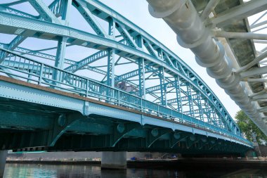 Açık gökyüzü yapısı altında nehir boyunca uzanan mavi çelik köprü