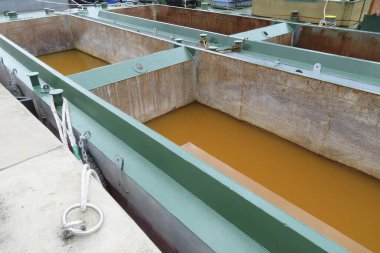 Kahverengi sıvı ve metalle dolu büyük sanayi tankları.