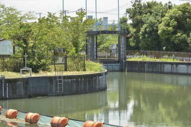 Sakin su, metal baraj kapısının yakınındaki ağaçları yansıtıyor.