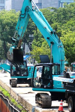 Yeşil ağaçlı inşaat sahasında çalışan kazıcılar