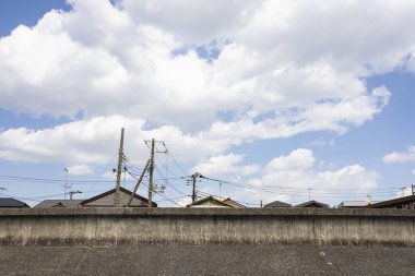 Çatıların üstündeki mavi gökyüzü ve beton duvarın arkasındaki elektrik direkleri.
