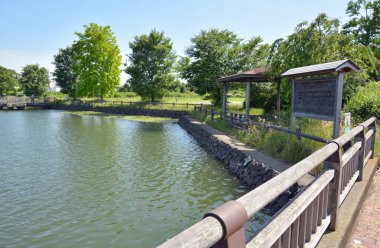 Sakin su, tahtadan yapılar ve patikalar yakınındaki ağaçları yansıtıyor.