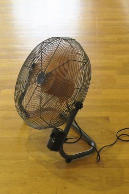 Tahta zeminde küçük siyah elektrikli vantilatör. 