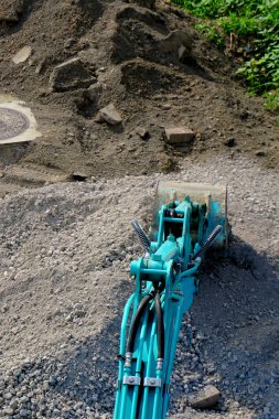 Mavi kazıcı, büyük toprak yığınının yanında çakıl kazıyor.