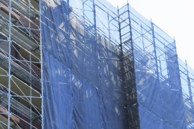 Mavi inşaat ağları ve metal iskelelerle kaplı uzun bir bina.