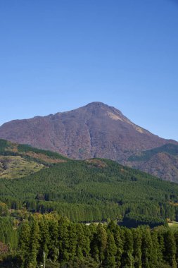Dağları, yemyeşil ormanı ve mavi gökyüzü olan güzel bir manzara.