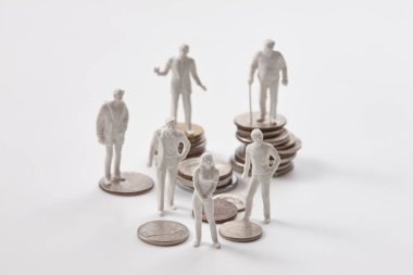 Beyaz arka planda madeni paraların üzerinde duran minyatür insanlar. İnsan heykelcikleri maket yapar