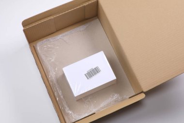 Üzerinde barkod olan beyaz kutu daha büyük bir karton kutunun içinde temiz bir filme sarılmış.