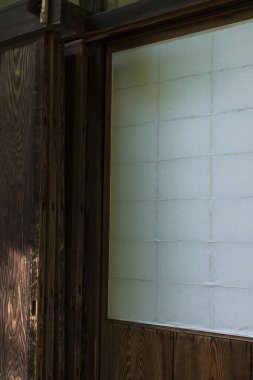 Güneş ışığı geleneksel ahşap duvara vuruyor, buzlu cam pencerenin yanında.