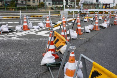 İnşaat bariyerlerinin yanında ıslak asfalt yolda turuncu trafik konileri var.