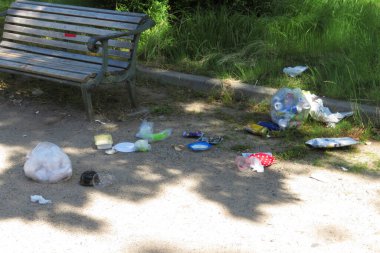 Güneşli öğleden sonra boş park bankının yanında dağınık çöp yığını