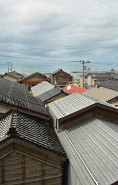 Bulutlu gökyüzünün altında, okyanus ufkunun yakınında üst üste binen çatılar.