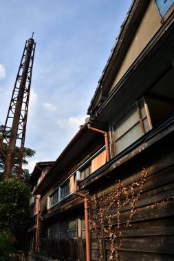 Yeşillik ve yüksek kuleyle çevrili eski ahşap bina.