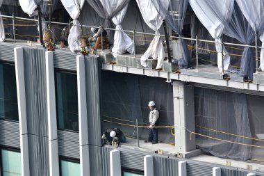 İnşaat işçileri harici bir binanın iskelesinde dikiliyorlar..