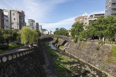 Taştan duvarlar ve mavi gökyüzünün altındaki binalar arasında akan şehir nehri.