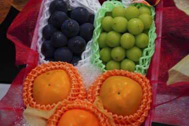 Koyu yeşil üzüm ve hurma da dahil olmak üzere çeşitli meyvelerin olduğu hediye sepeti, genellikle meyve sepeti olarak adlandırılır..