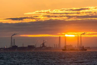 Petrol rafinerisi ve deniz kıyısında gün batımında     