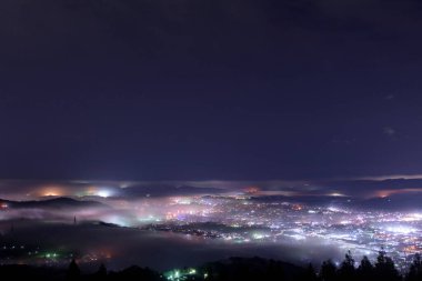 Aydınlanmış şehrin güzel gece manzarası ve sisli karanlık tepeler 