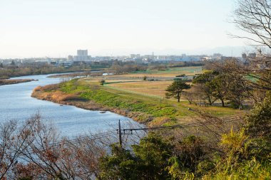 Nehir, uzak şehrin ufuk çizgisi yakınlarındaki çimenli tarlalarda kıvrılıyor.