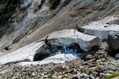 Eriyen buzullar güneş ışığı altında kayalık dağ manzarasından aşağı akıyor.