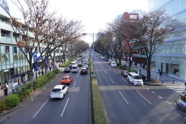 Japon şehrindeki işlek bir caddenin yüksek açılı görüntüsü. Çeşitli arabaları ve sarı bir merkezi var. Yokuş yukarı gidiyor.