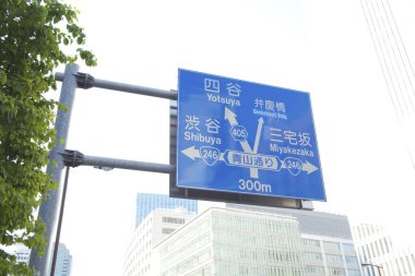 Japon karakterleri şehir binalarına karşı mavi yol işareti