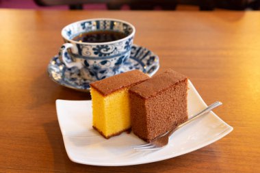 Kahve fincanının yanında bir dilim Castella keki.