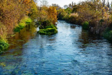 Güneşli bir günde sonbahar parkında güzel bir nehir ve ağaç manzarası.