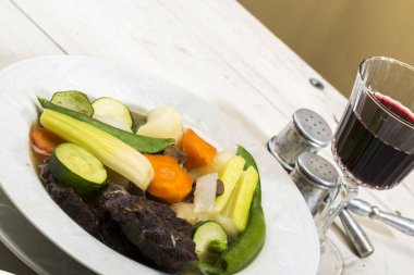 Şarap ve sebzeli et, beyaz tabakta. 