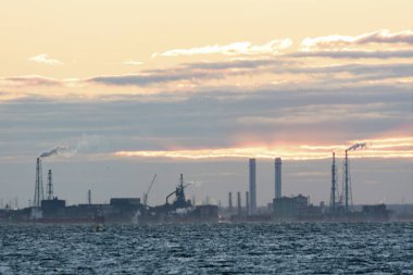 Petrol rafinerisi ve deniz kıyısında gün batımında     