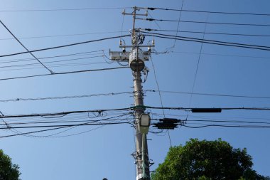 Açık mavi gökyüzüne karşı elektrik kablolarını destekleyen elektrik direği